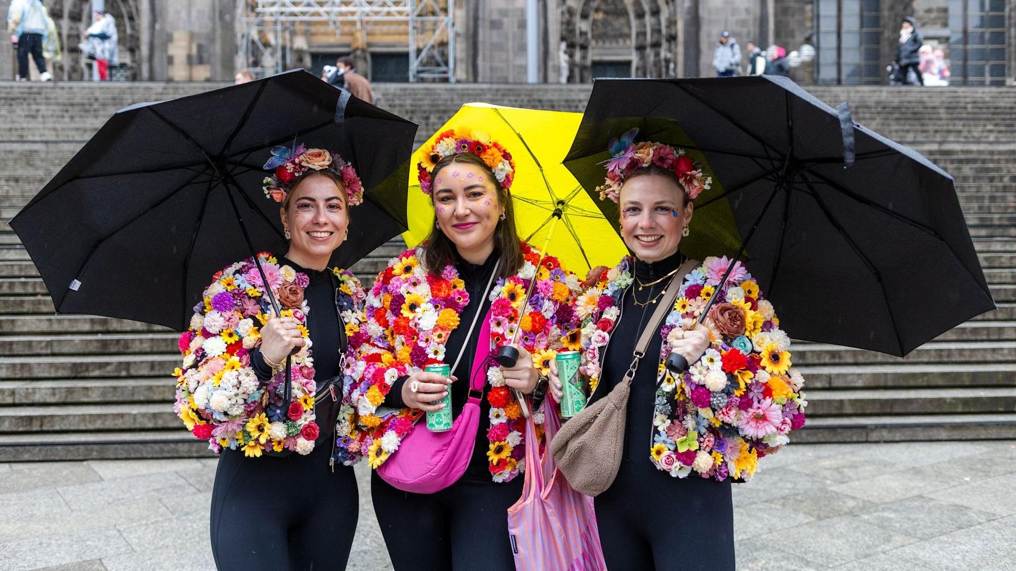 Drei Frauen mit Regenschirmen und bunten Blumenjacken.