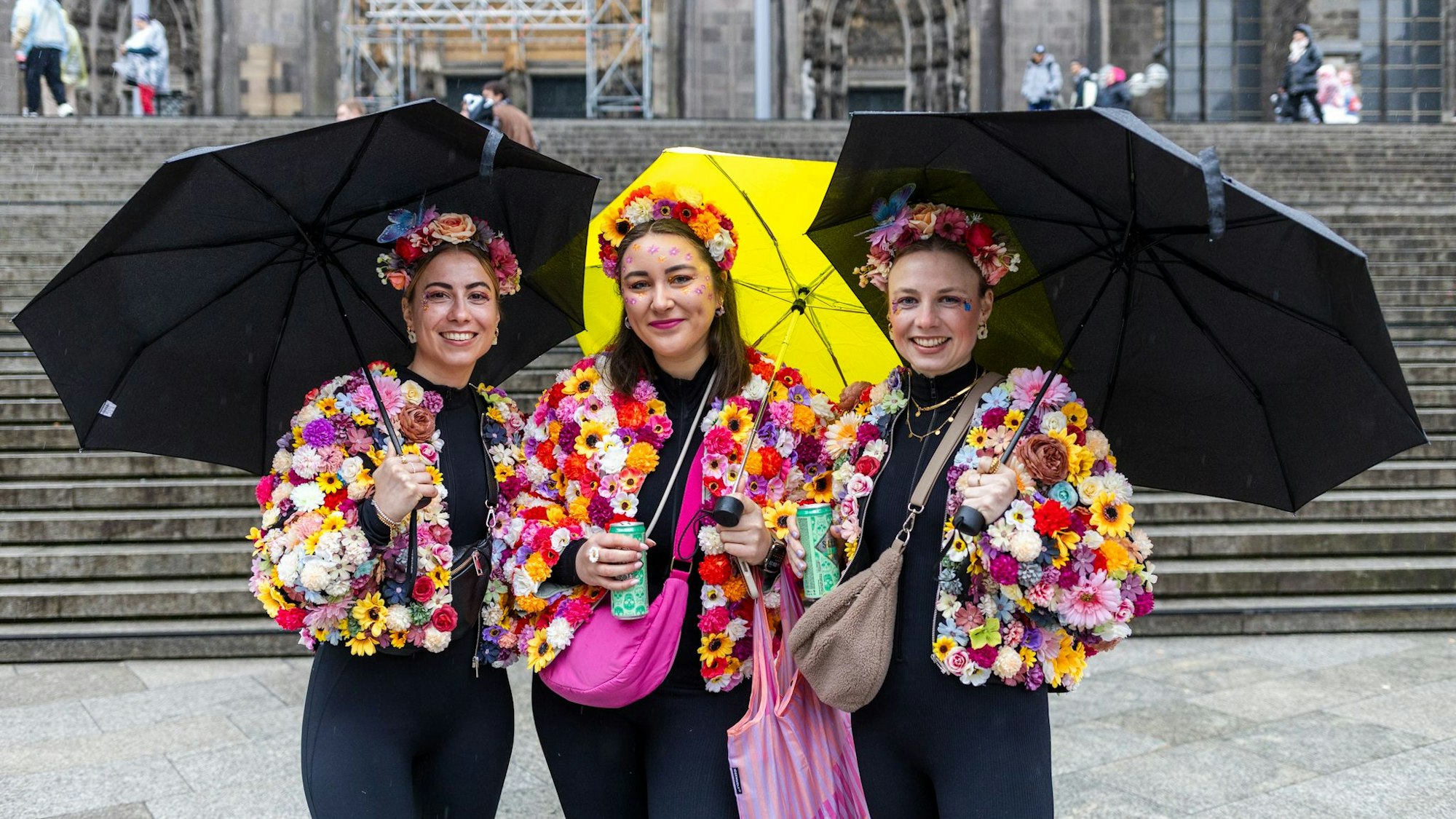 Drei Frauen mit Regenschirmen und bunten Blumenjacken.