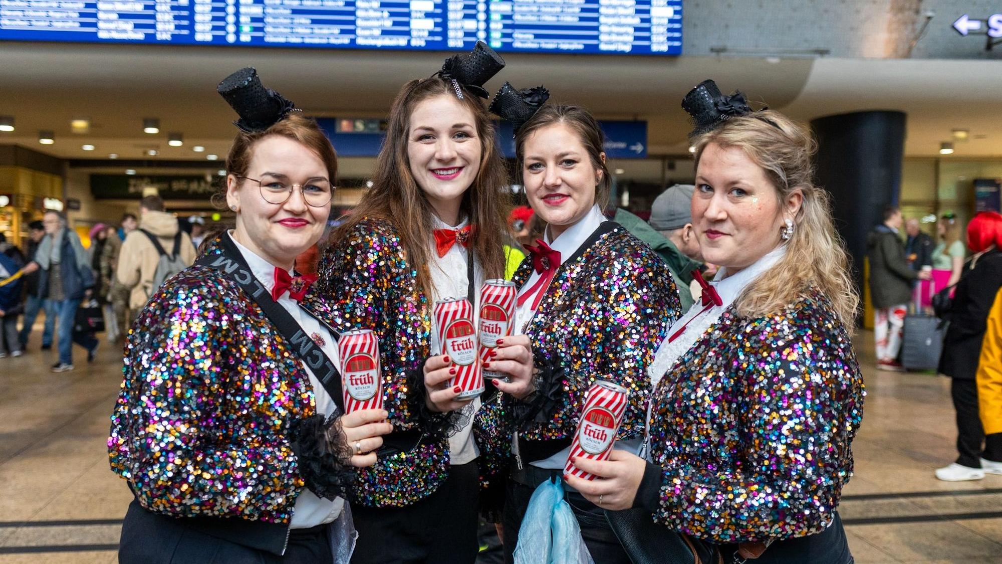 Vier Frauen tragen glitzernde Jacken und einen kleinen Zylinder auf dem Kopf.
