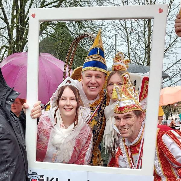 Zwei Karnevalsprinzen im Ornat und zwei Prinzessinnen schauen durch einen Bilderrahmen.