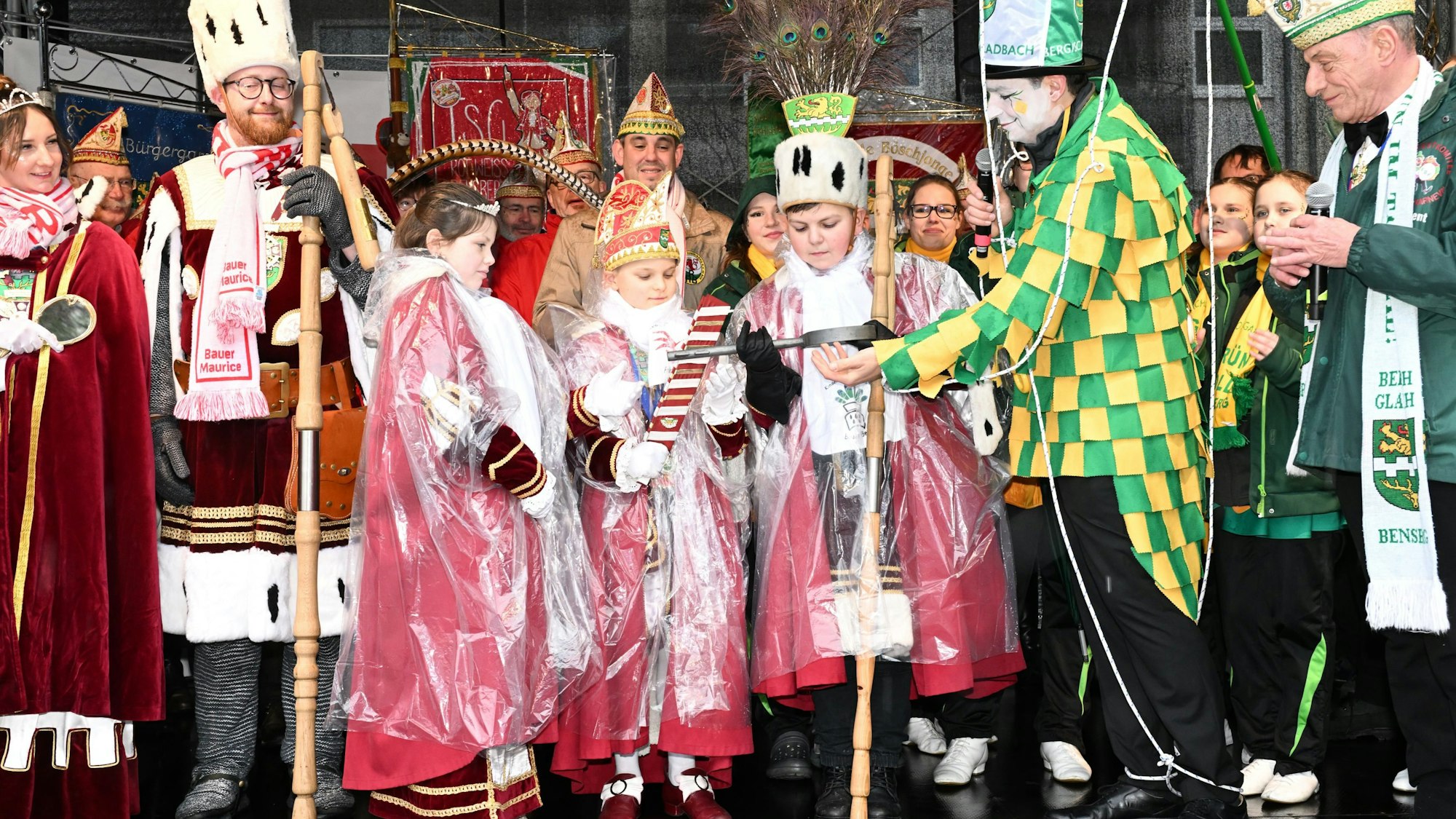 Das Kinderdreigestirn steht auf der Bühne, rechts neben ihnen der als Marionette kostümierte Bürgermeister, der ihnen in seiner Hand den großen Stadtschlüssel reicht.