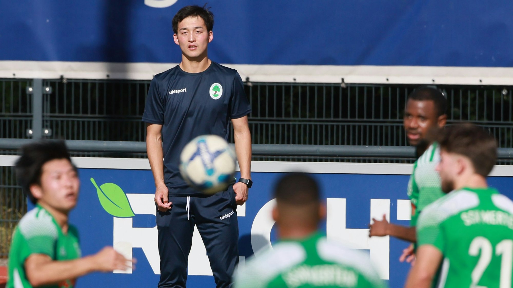 Das Foto zeigt den Königsdorfer Trainer Takahito Ohno, der von der Seitenlinie auf das Spiel vor ihm schaut.