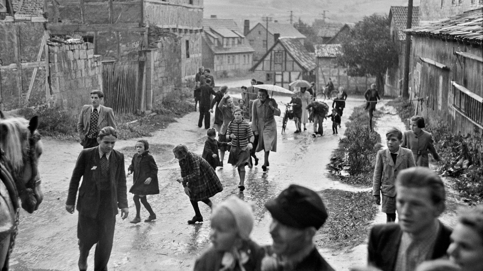 Menschen gehen über eine verregnete Dorfstraße.
