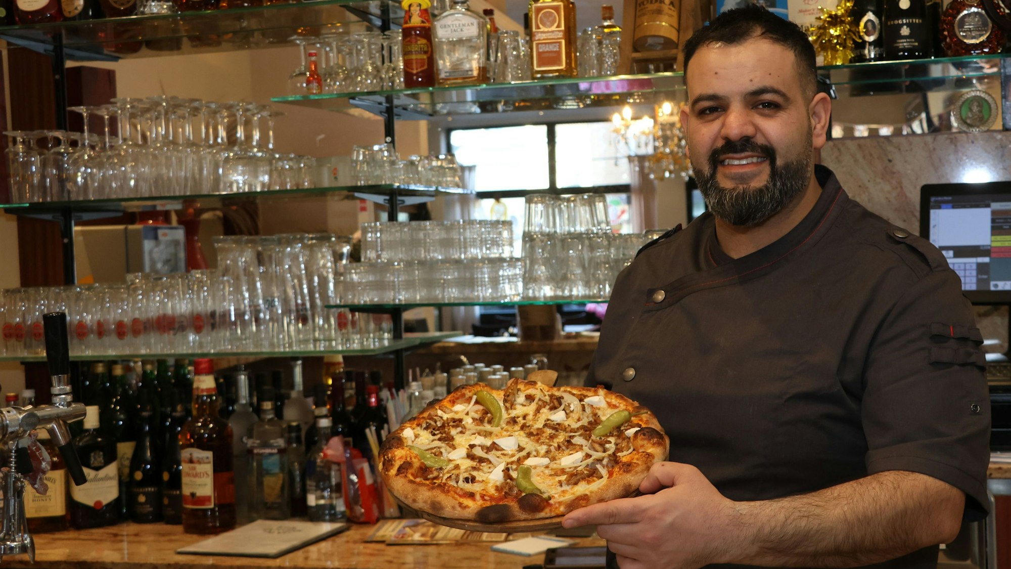 Auf dem Bild ist ein Mann mit einer frisch gebackenen Pizza zu sehen.