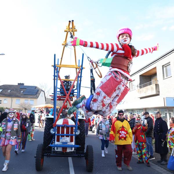 Ein bunter Clown hängt an einer Konstruktion an einem Traktor und „fliegt“ so im Karnevalszug in Bad Honnef.