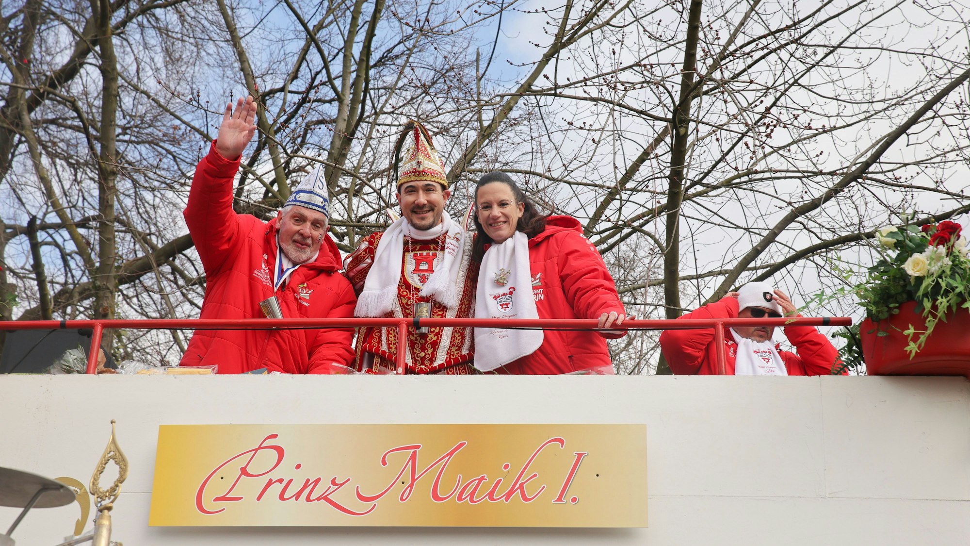 Zwei Männer und eine Frau grüßen vom Karnevalswagen.