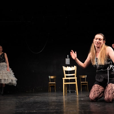 Eine Frau kniet auf der Bühne, eine andere schaut zu.