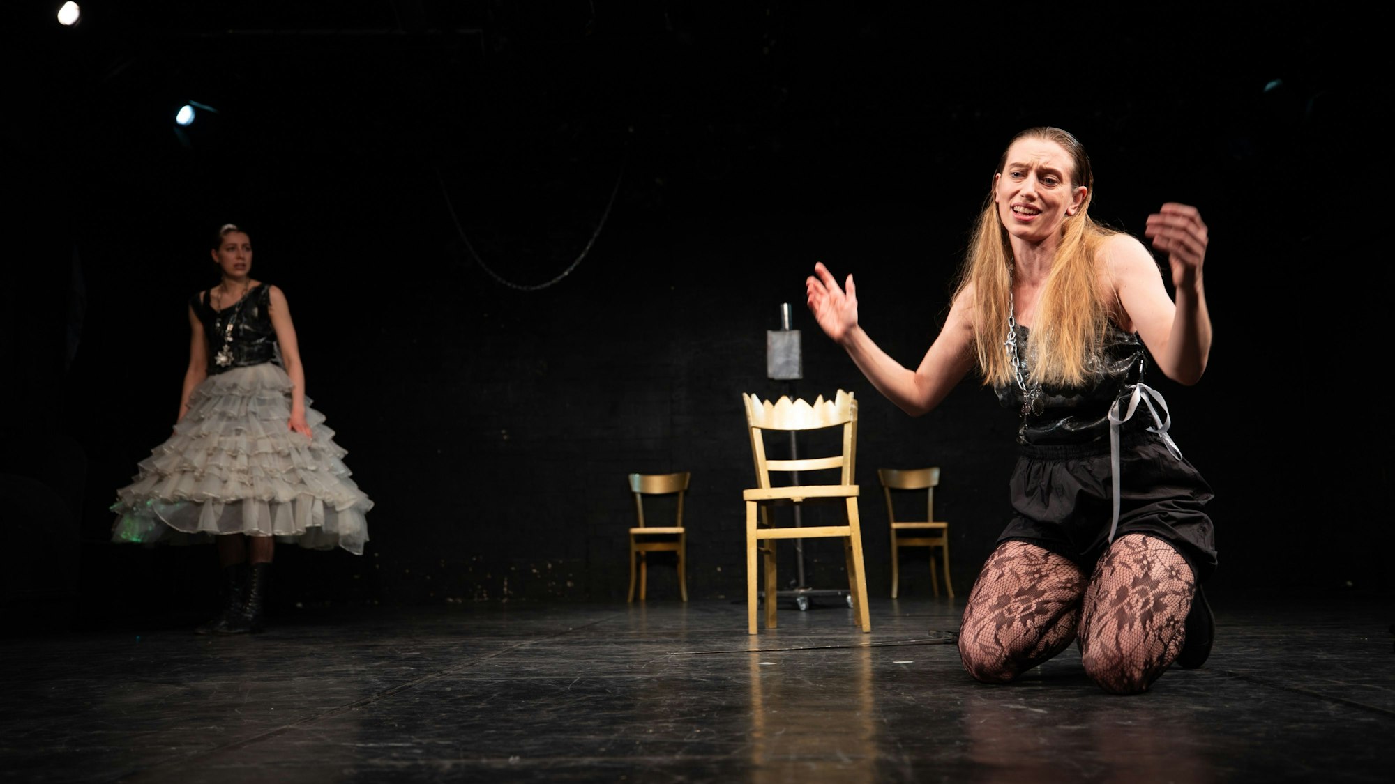 Eine Frau kniet auf der Bühne, eine andere schaut zu.