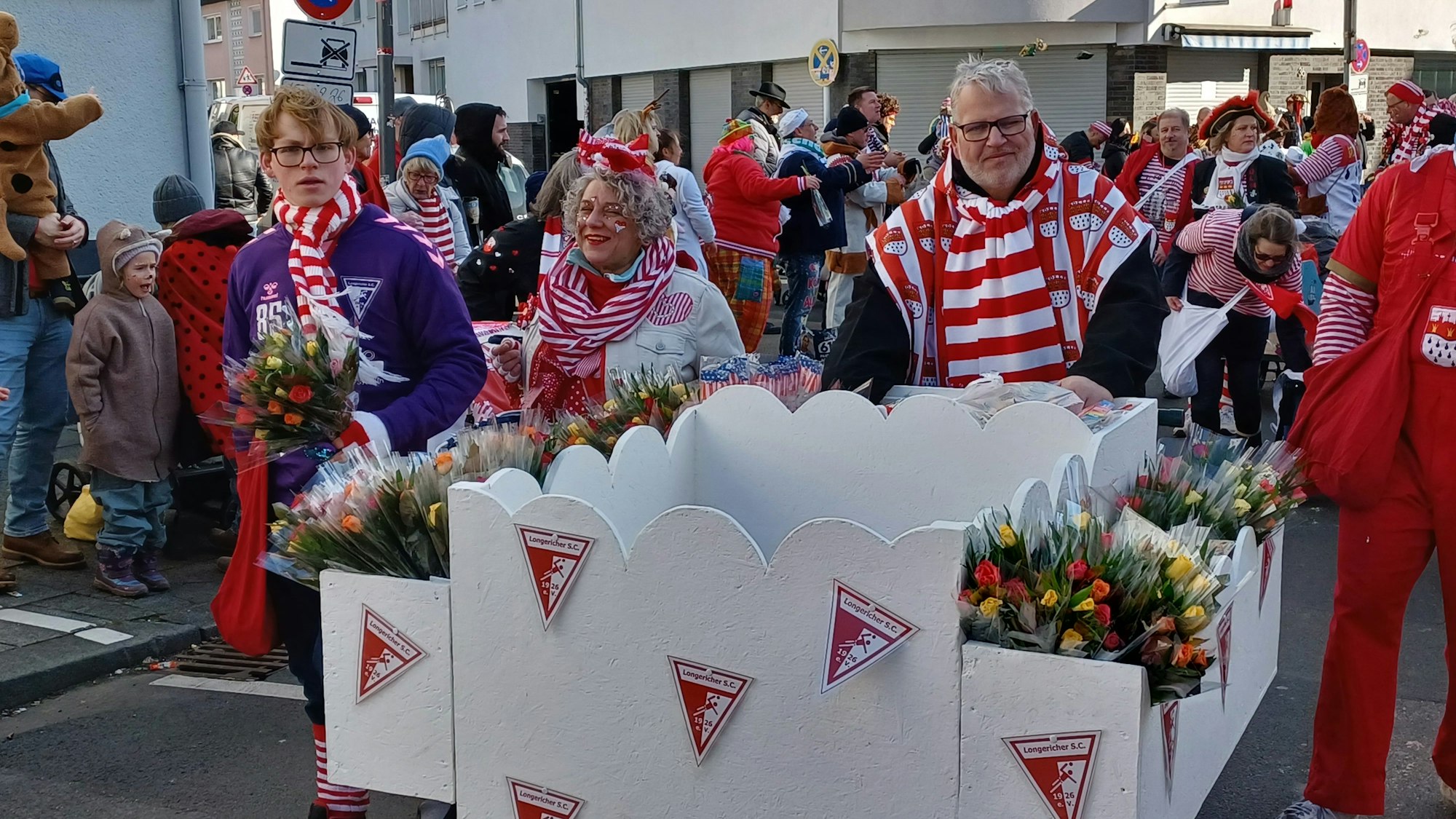 Ein Wagen mit Strüßjer, begleitet von Karnevalisten in Rot-Weiß