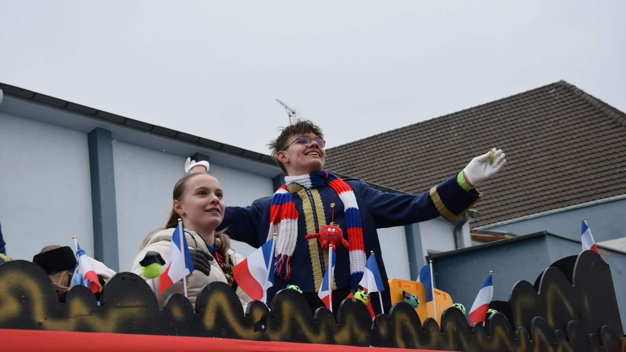 Auf einem Karnevalswagen stehen ein Mann und und eine Frau mit französischen Flaggen.