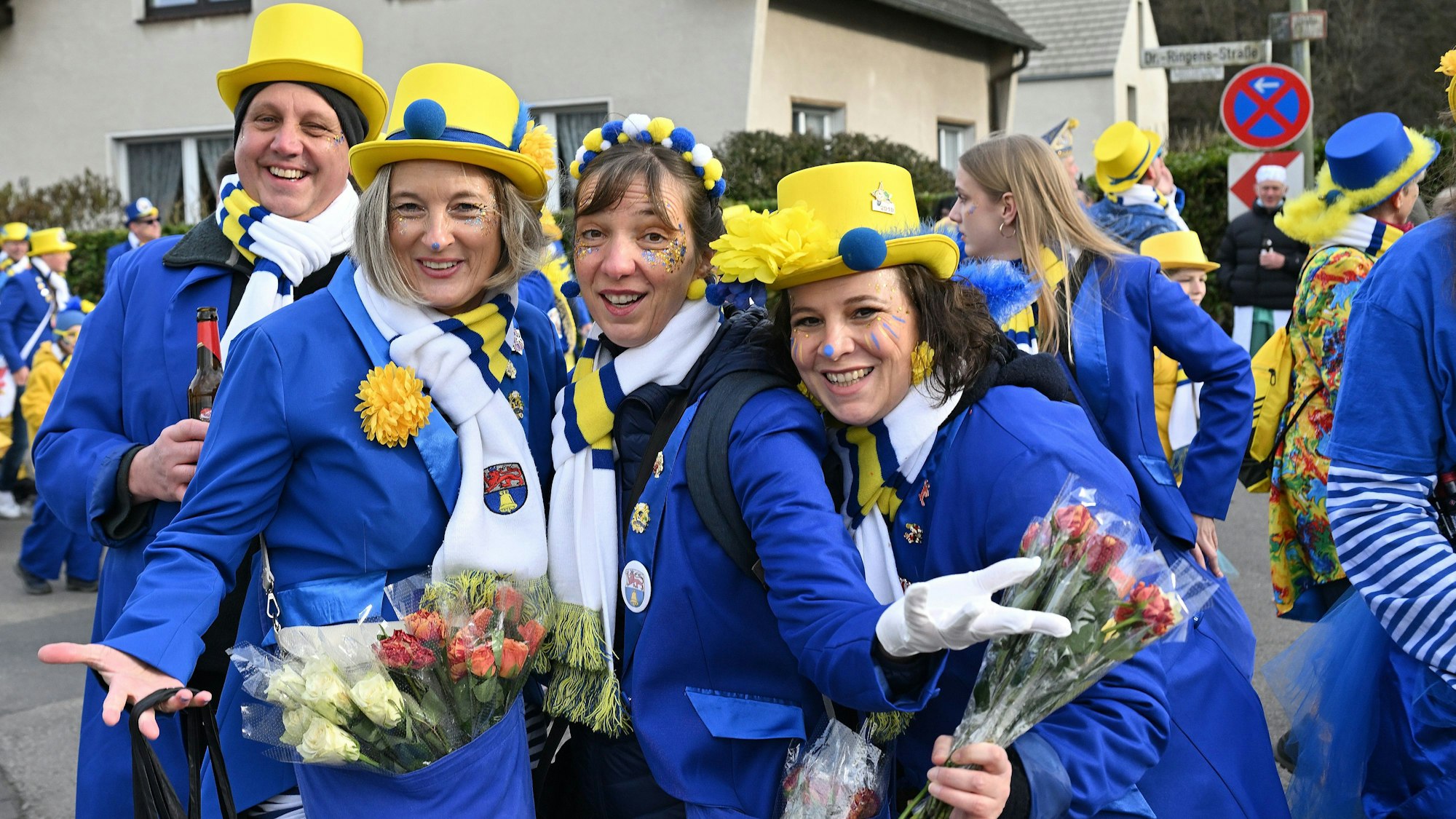 Eine Gruppe Karnevalisten trägt einen blau-gelben Anzug und hat Strüssjer und eine Flasche Bier dabei.