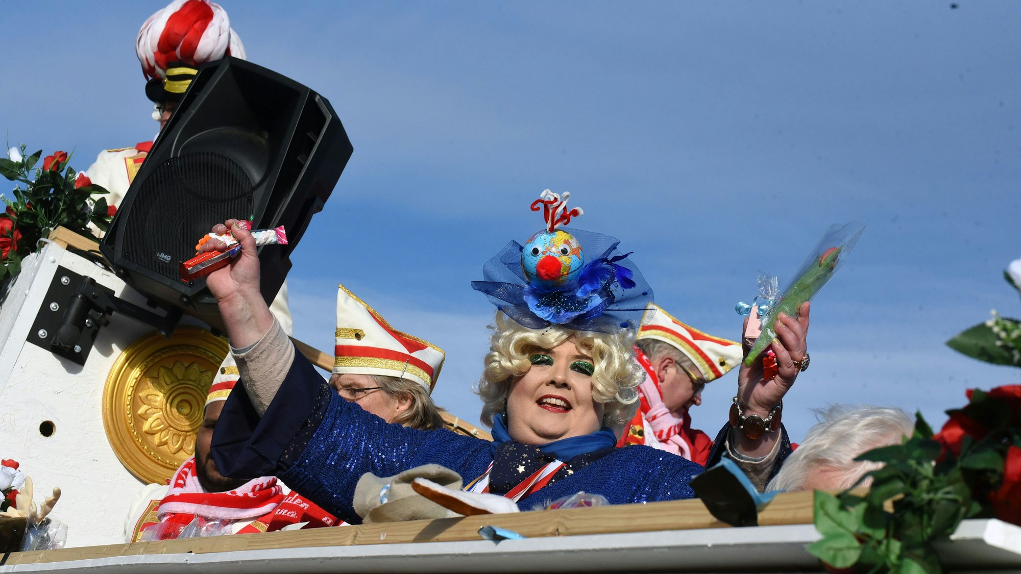 Eine Jecke schmeißt Kamelle von einem Karnevalswagen.