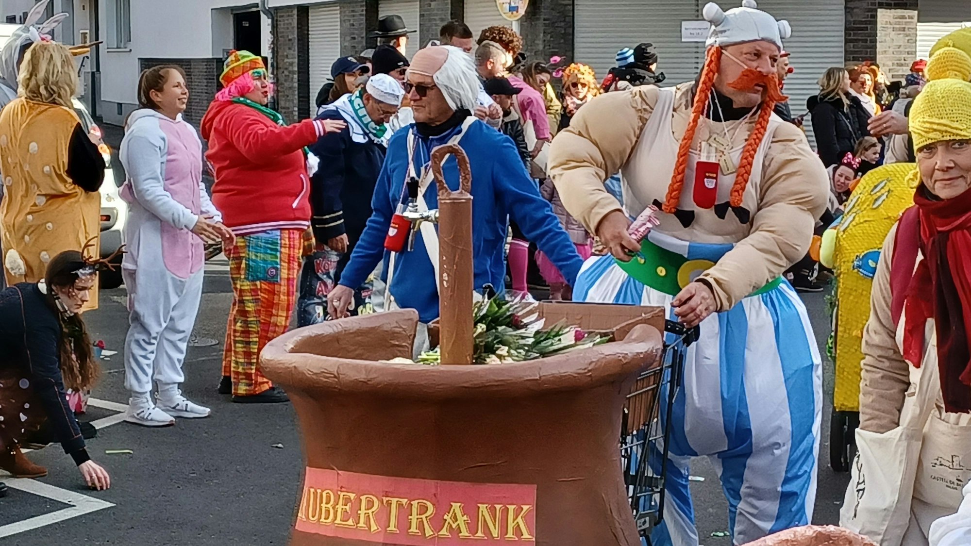 Ein als Obelix verkleideter Mann hat einen Wagen in Form eines Kessels Zaubertrank dabei. Darin sind Strüßjer.