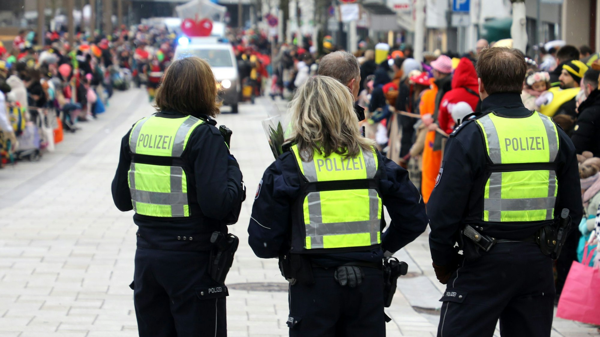 Polizeibeamtinnen und -beamte stehen vor dem Karnevalszug in der Bensberger Schloßstraße.