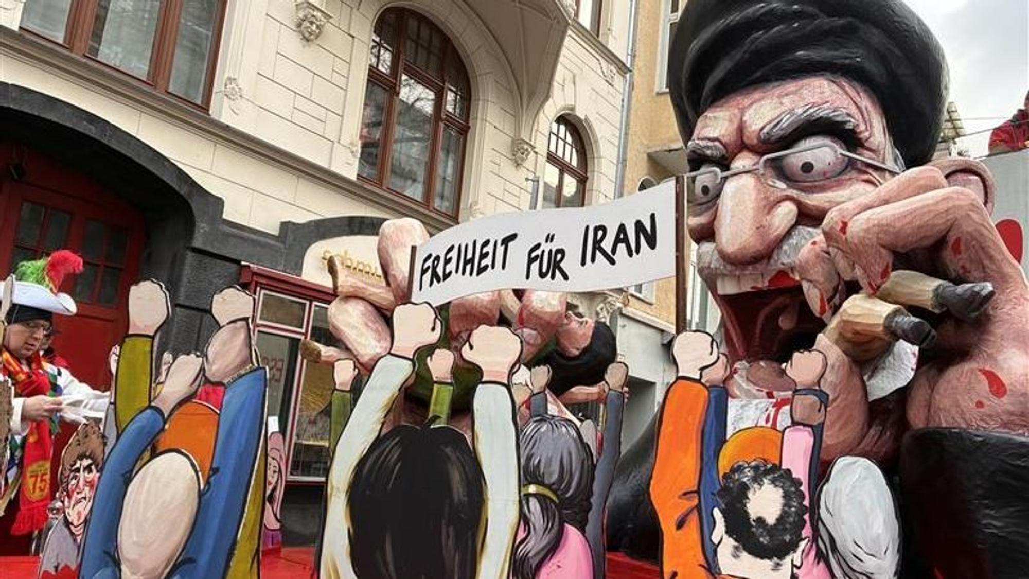 Das Bild zeigt den Wagen beim Kölner Rosenmontagszug, der den iranischen Politiker und Religionsführer Ali Chamenei zeigt. Blutrünstig verschlingt er sein Volk.