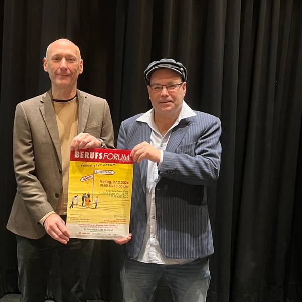 Ein großer Mann mit Glatze und einer mit Mütze und Brille halten zusammen ein Plakat hoch, das auf das Berufsforum in Porz hinweist.