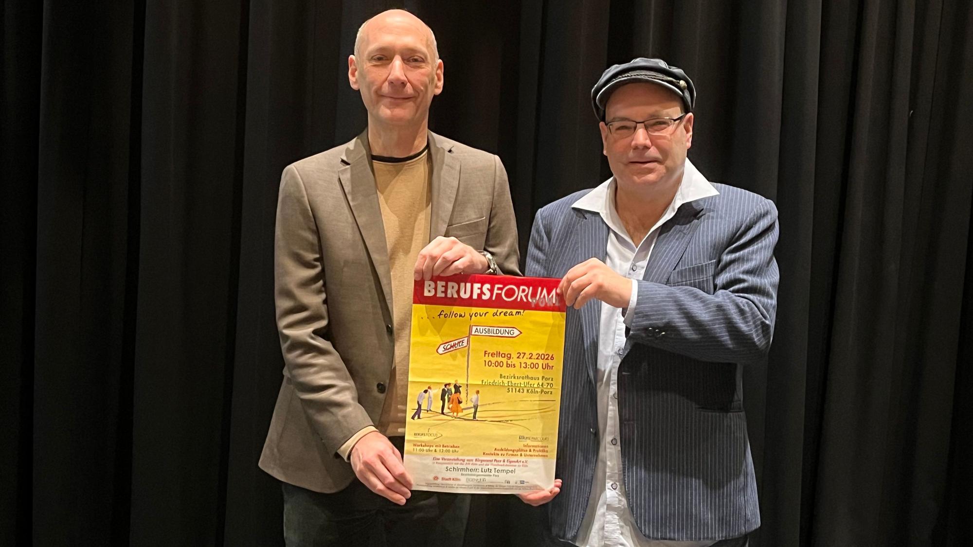 Ein großer Mann mit Glatze und einer mit Mütze und Brille halten zusammen ein Plakat hoch, das auf das Berufsforum in Porz hinweist.