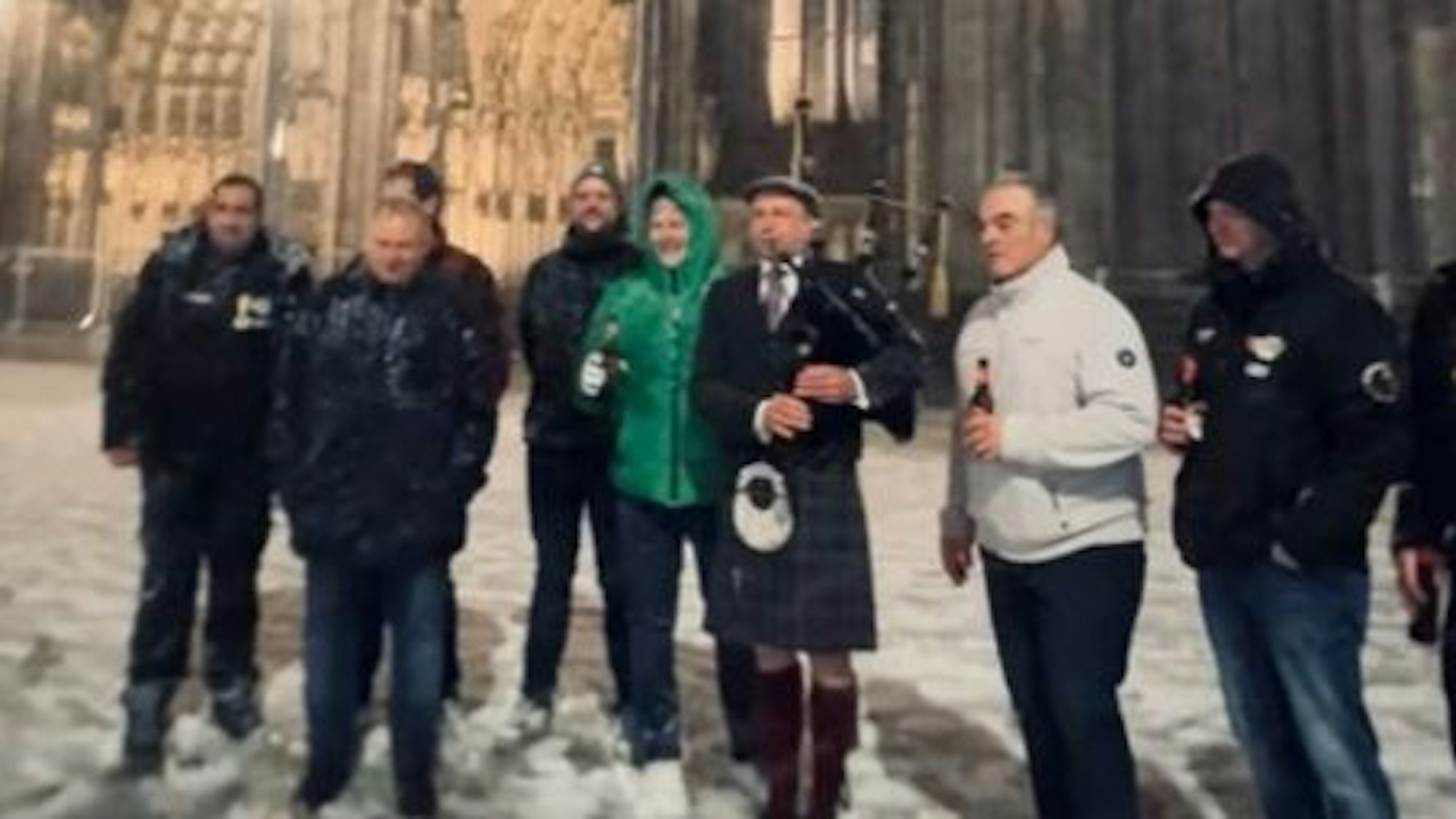 Ein Dudelsackspieler musiziert vor dem Kölner Dom, umgeben von mehreren Personen.
