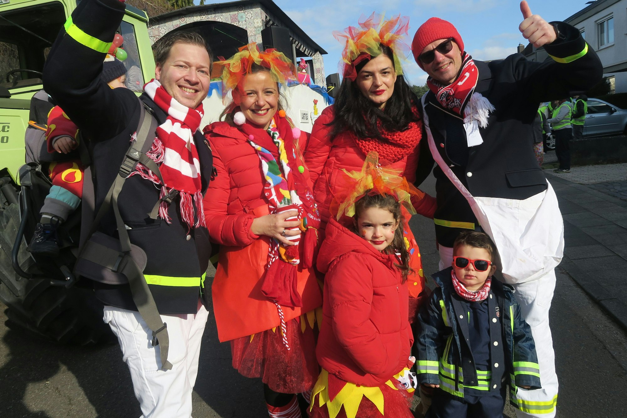 Rot gekleidete Jecke, zum Teil in Feuerwehrjacken lachen in die Kamera.