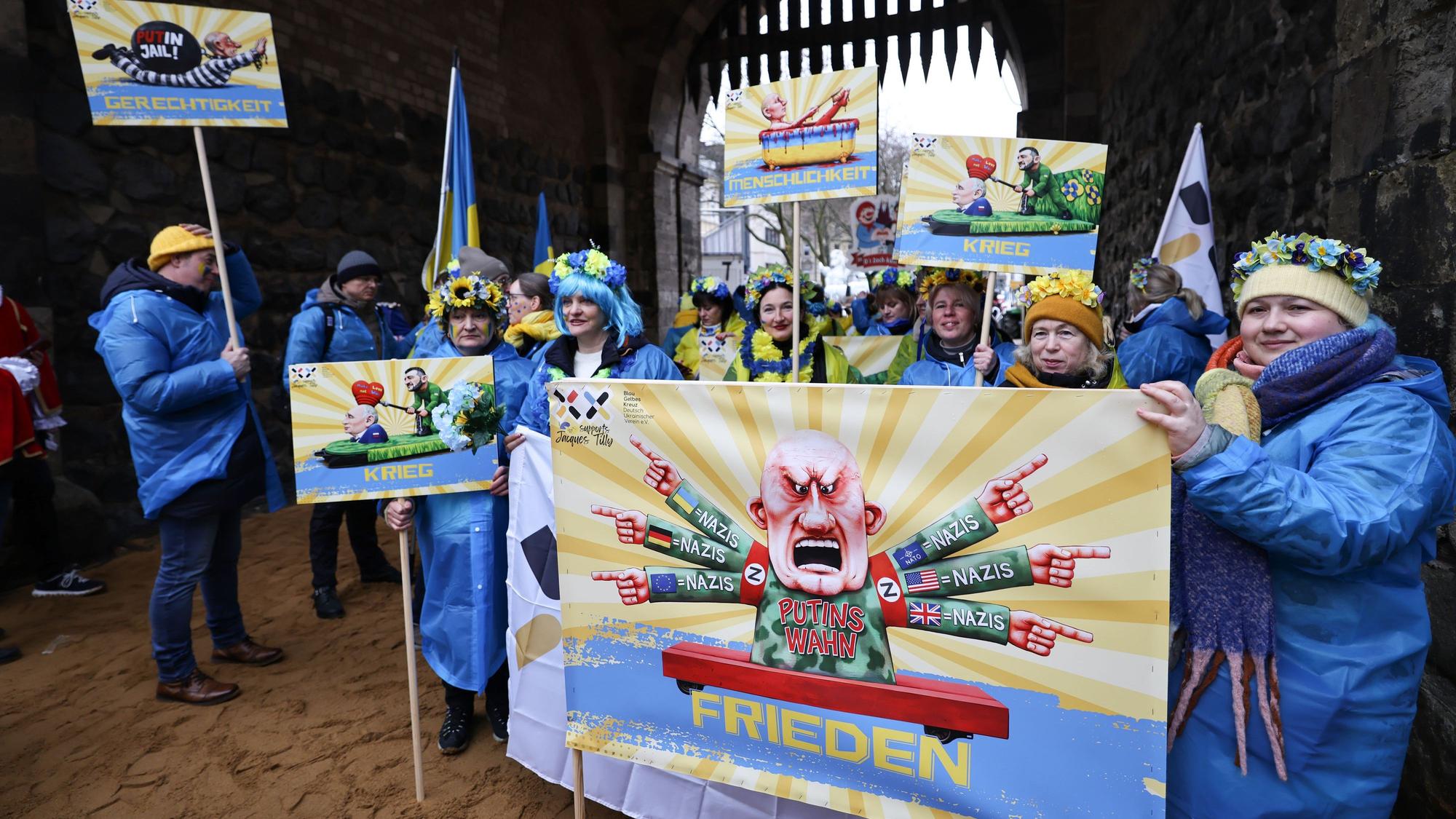 Karnevalisten des Blau-Gelben Kreuzes tragen ein Schild eines früheren Satiremotivs von Jacques Tilly.