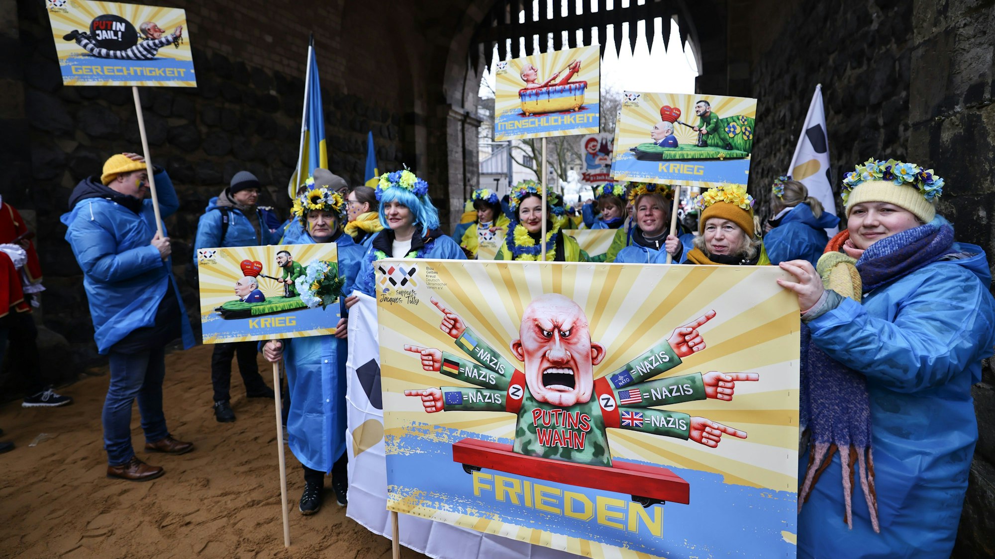 Karnevalisten des Blau-Gelben Kreuzes tragen ein Schild eines früheren Satiremotivs von Jacques Tilly.