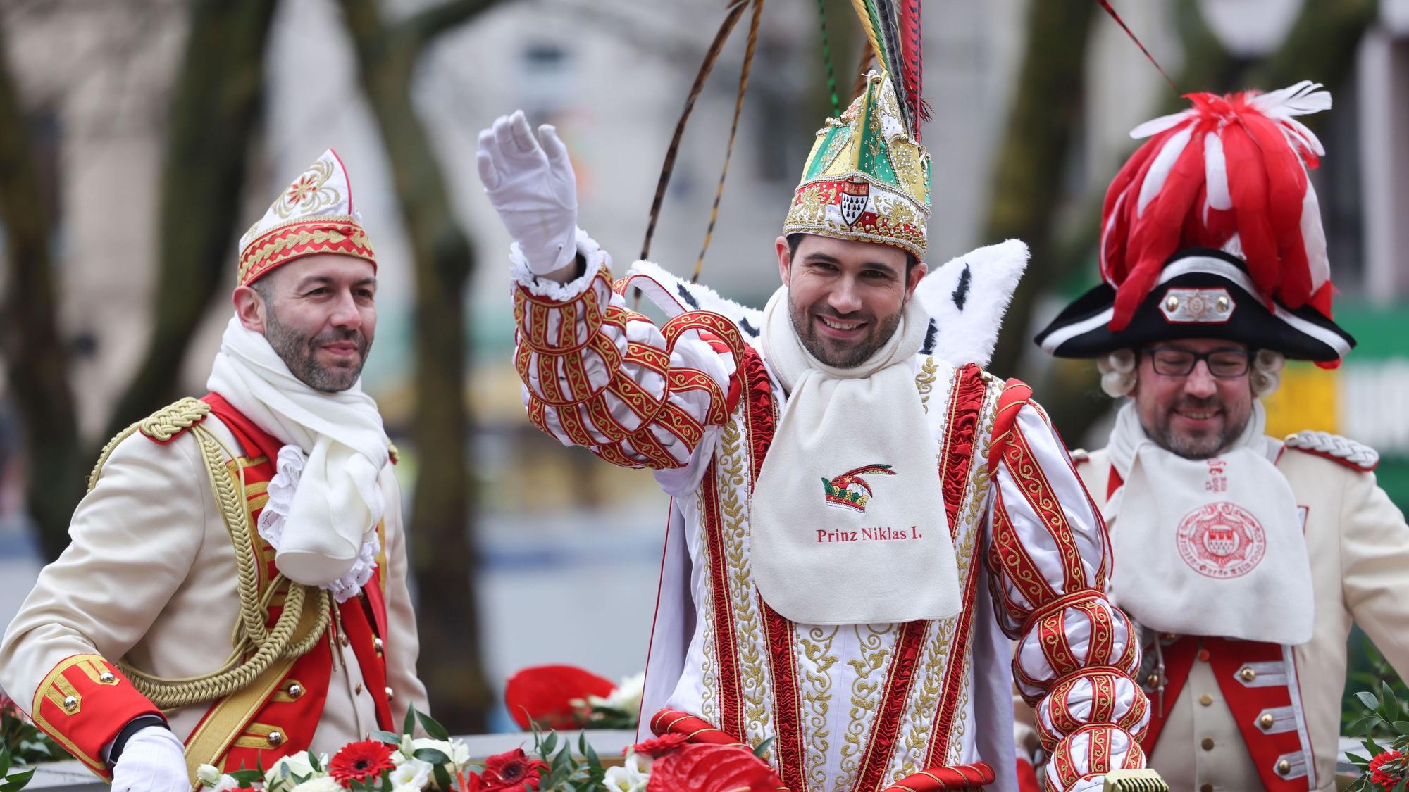 Prinz Niklas I. (M) winkt den Karnevalisten am Straßenrand beim Rosenmontagszug in Köln zu.