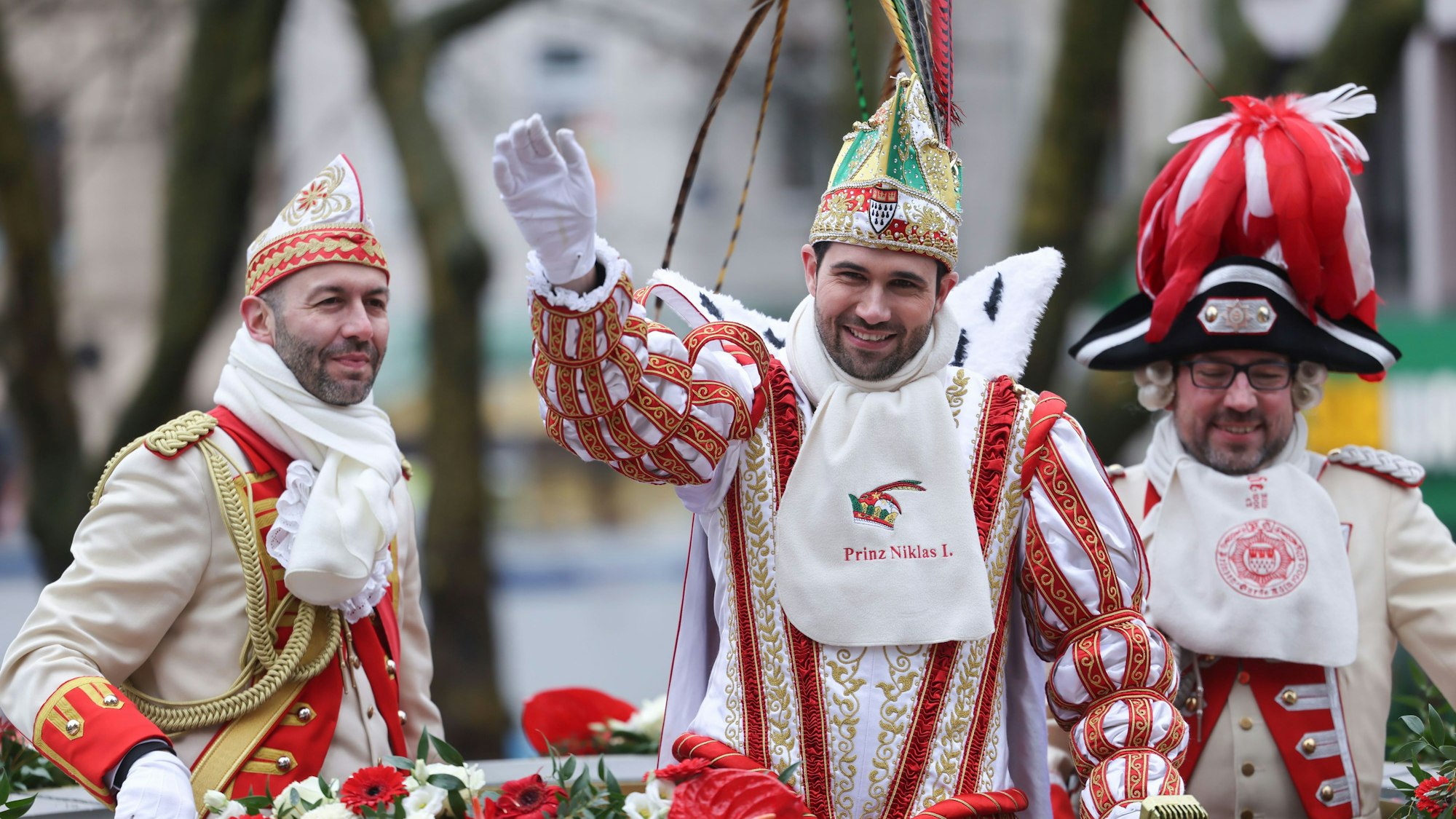 Prinz Niklas I. (M) winkt den Karnevalisten am Straßenrand beim Rosenmontagszug in Köln zu.