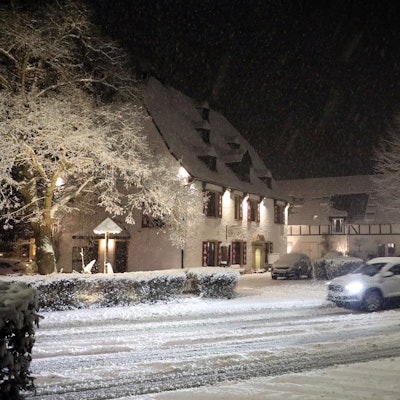 Ein Auto fährt auf einer schneebedeckten Straße an der Malteser Komturei in Bergisch Gladbach-Herrenstrunden vorbei.