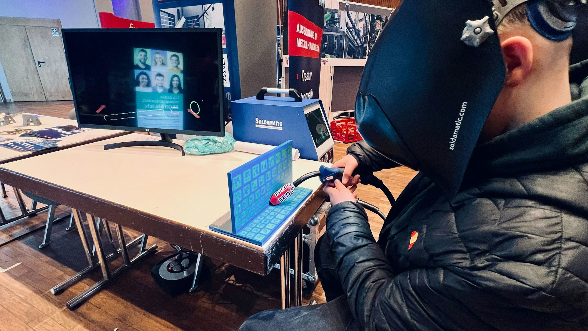 Ein junger Mann hat eine Maske vor dem Gesicht und ein Schweißgerät in der Hand. Eine Arbeitsaktion wird mit den Geräten simuliert.