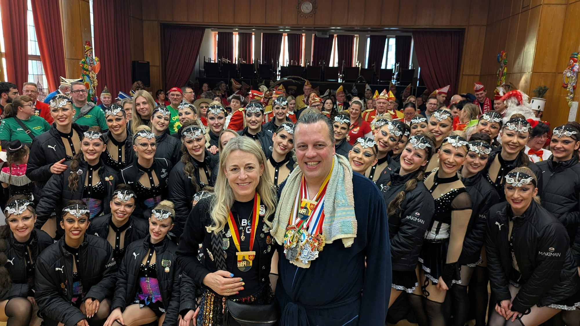 Der Bürgermeister und die Geehrte stehen nebeneinander, hinter ihnen Tänzerinnen und andere Gäste.