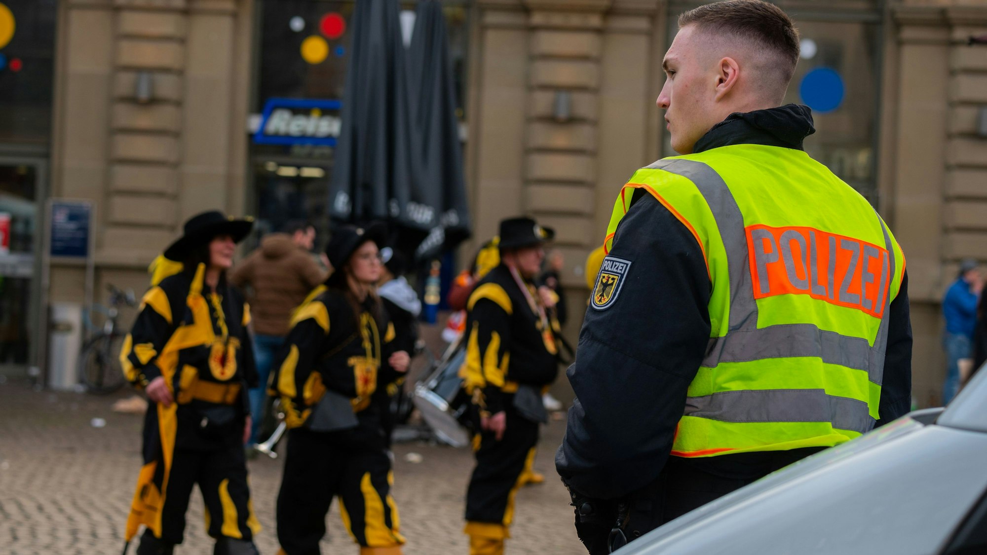 Ein Polizist beobachtet auf dem Bahnhofsvorplatz das närrische Treiben bei einem Rosenmontagszug.