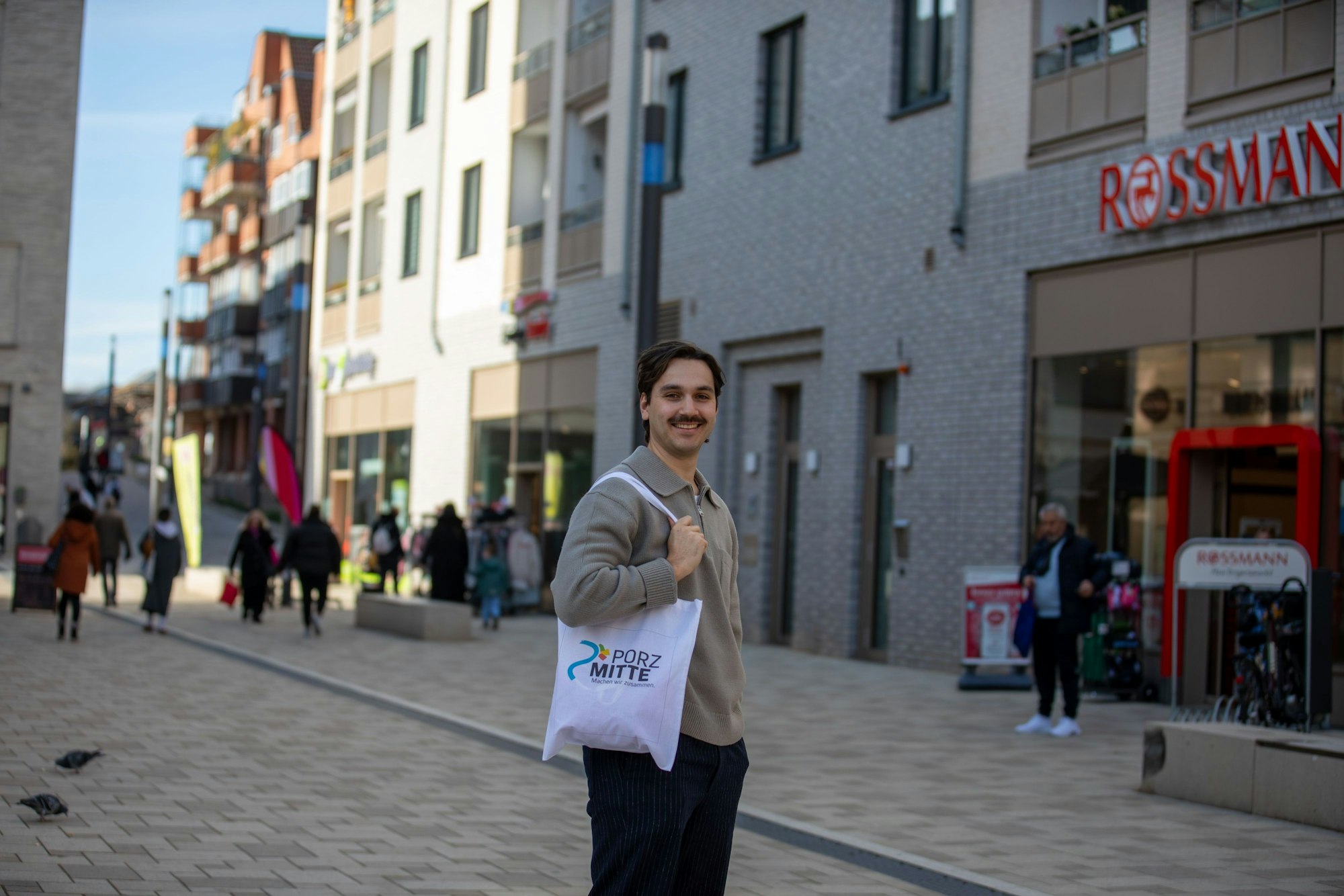 Ein Mann steht mit einem Stoffbeutel über der Schulter in der Porzer Innenstadt.