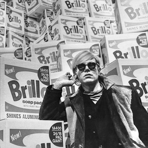Andy Warhol lehnt an einem Stapel Verpackungen für Putzschwämme.