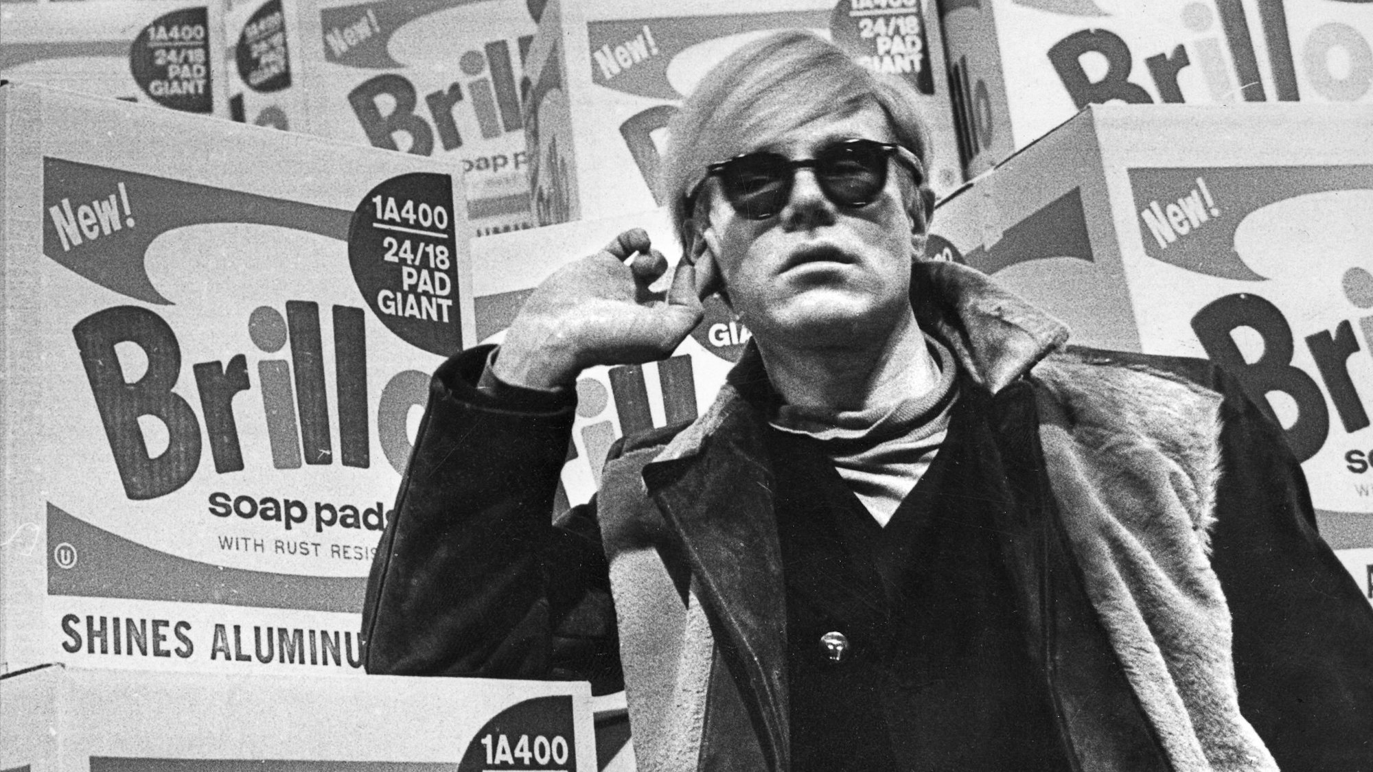 Andy Warhol lehnt an einem Stapel Verpackungen für Putzschwämme.