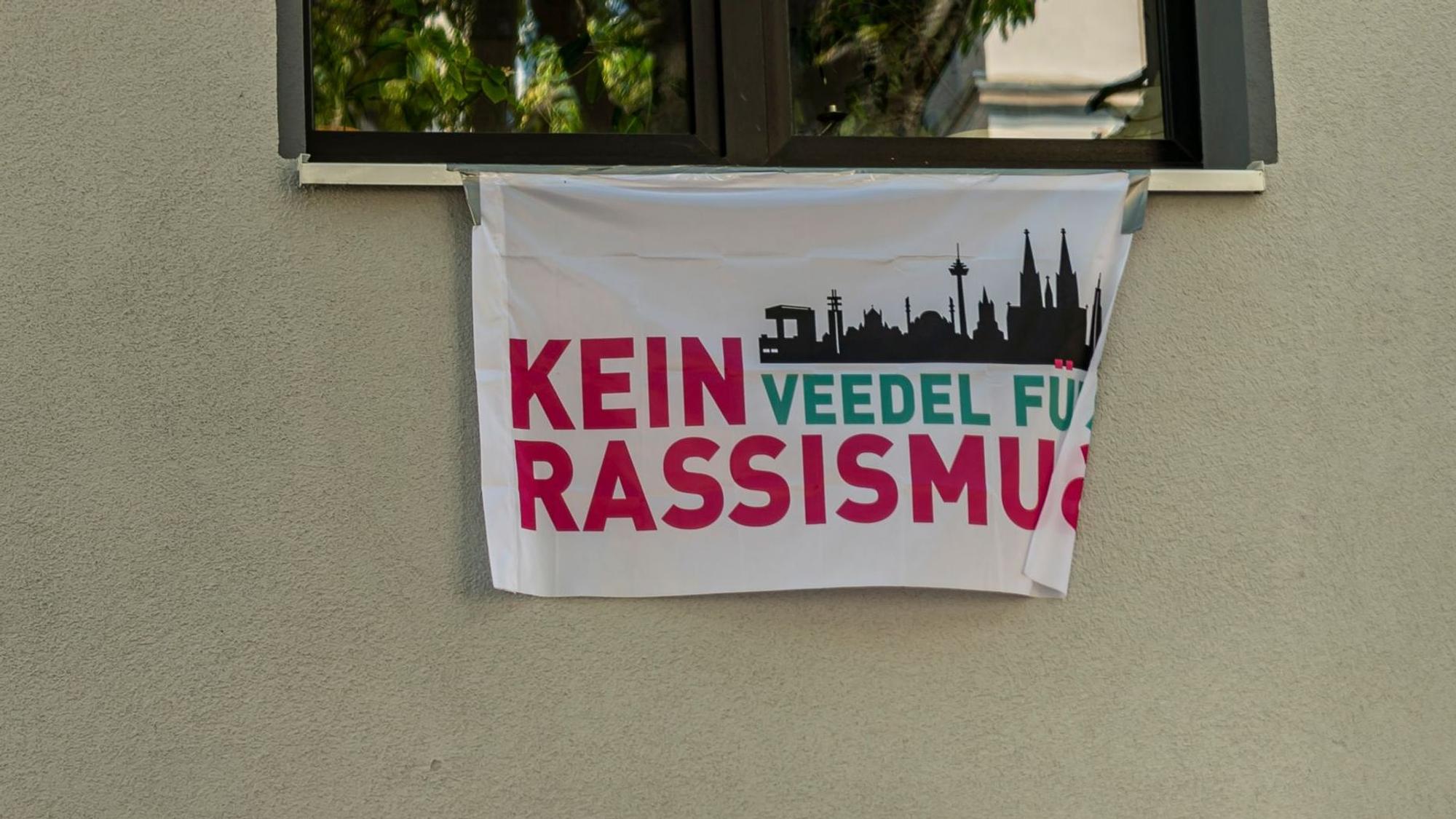 Das Bild zeigt eine Fahne mit der Aufschrift „Kein Veedel für Rassismus“.