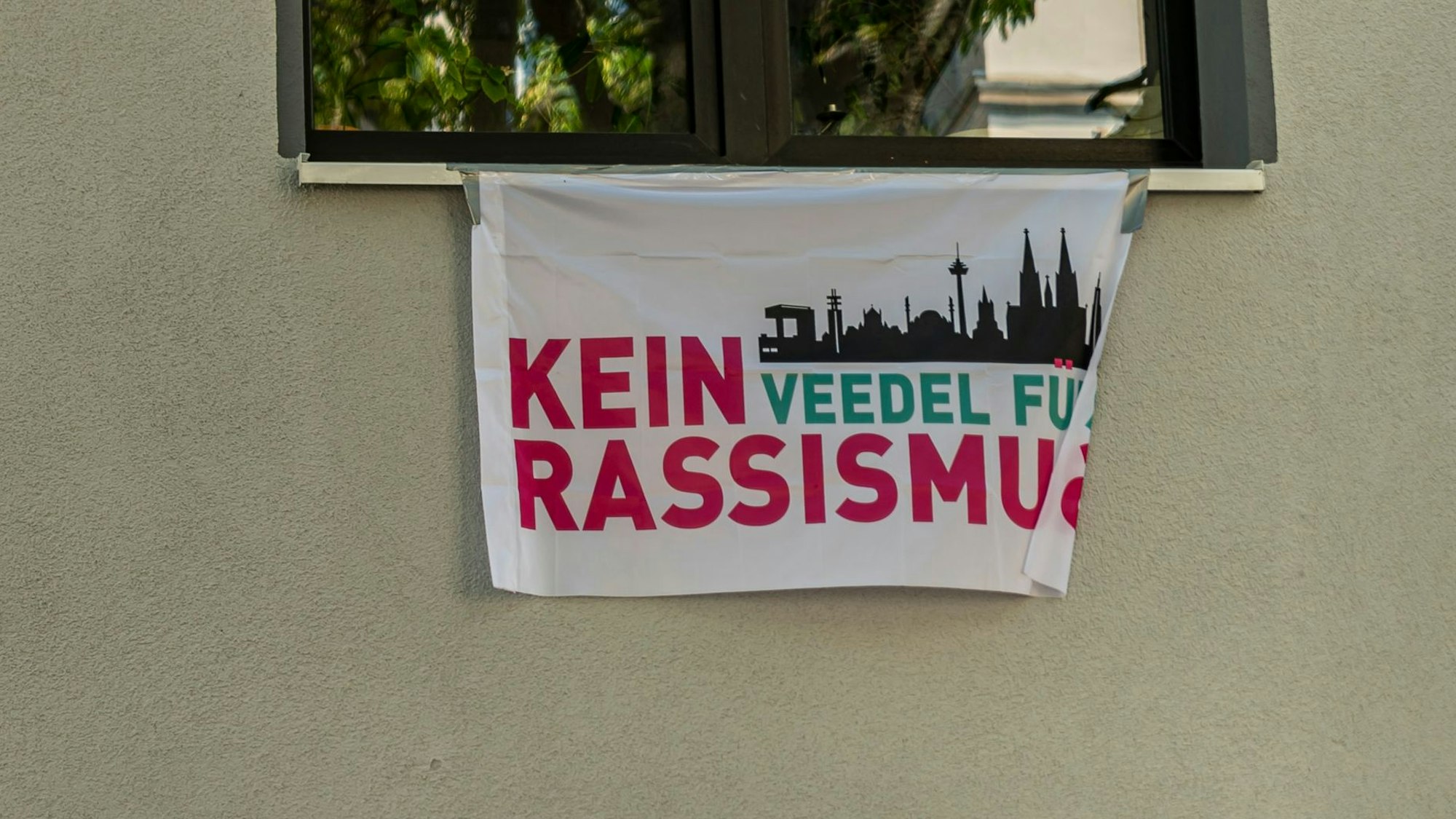 Das Bild zeigt eine Fahne mit der Aufschrift „Kein Veedel für Rassismus“.