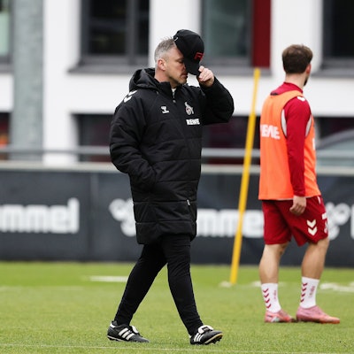 Lukas Kwasniok hält sich beim Training des 1. FC Köln seine Kappe vor das Gesicht.