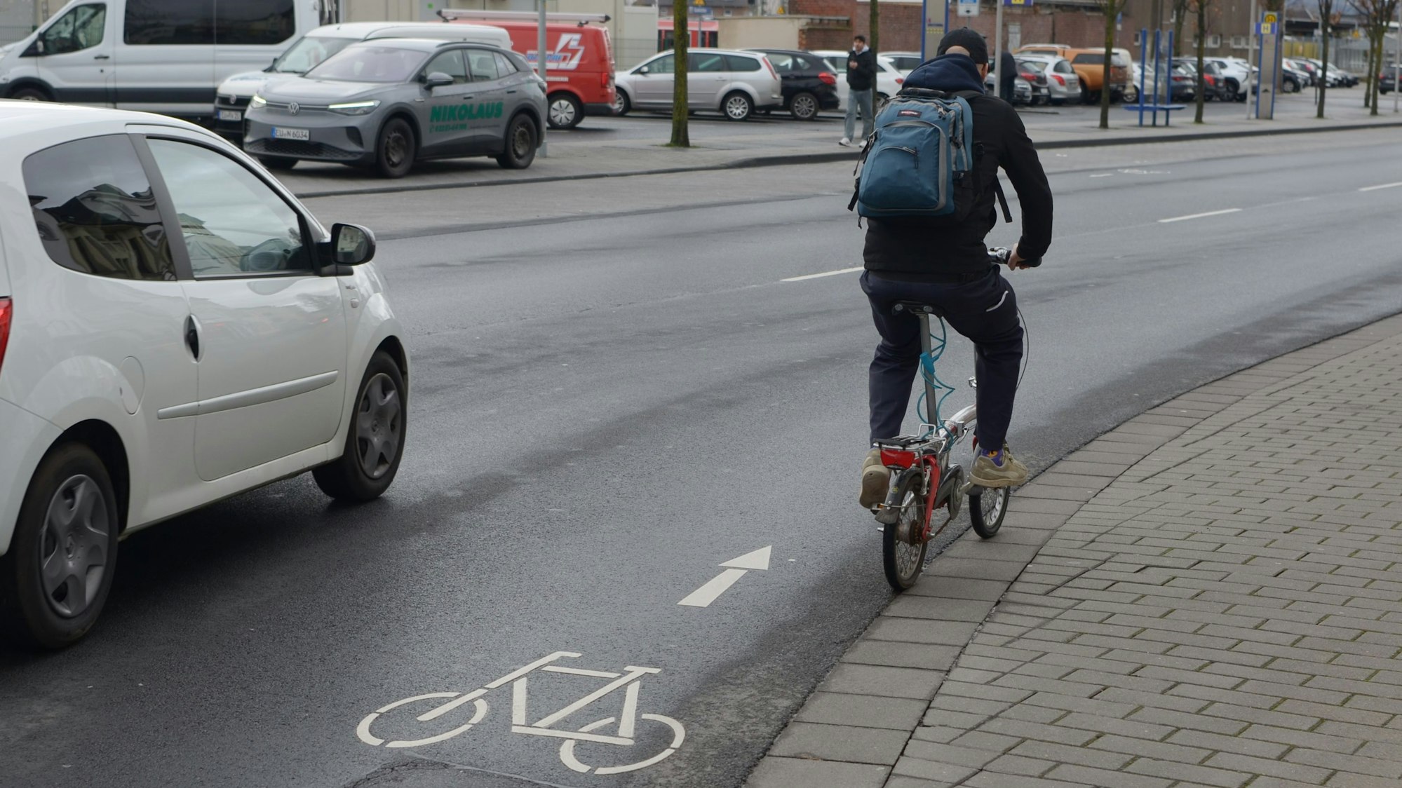 Ein Radfahrer passiert eine Stelle mit einem Fahrradpiktogramm, neben ihm ein Auto.