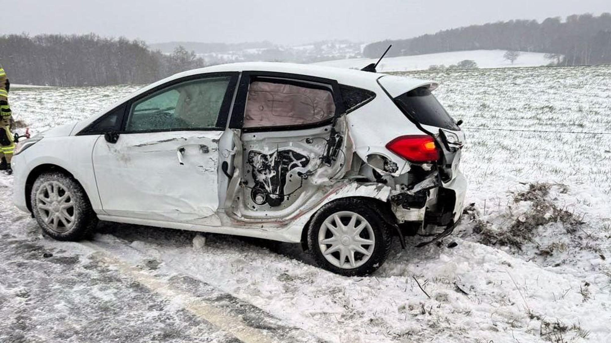 Ein beschädigtes Unfallauto steht an einer winterlichen Straße.