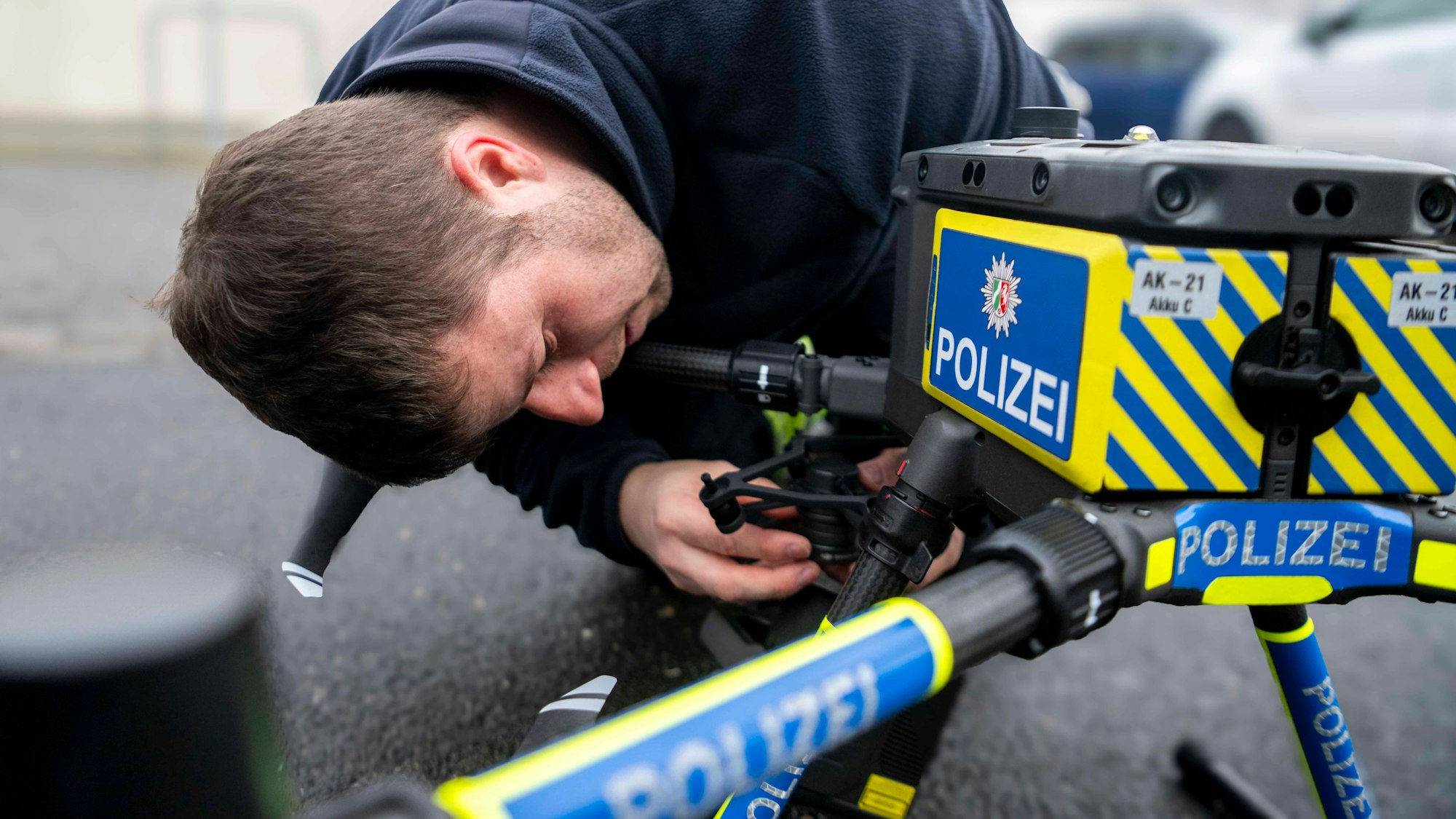Das Bild zeigt den Polizei-Mitarbeiter, der die Kamera an die mit Polizei-Aufklebern versehehe Drohne schraubt.