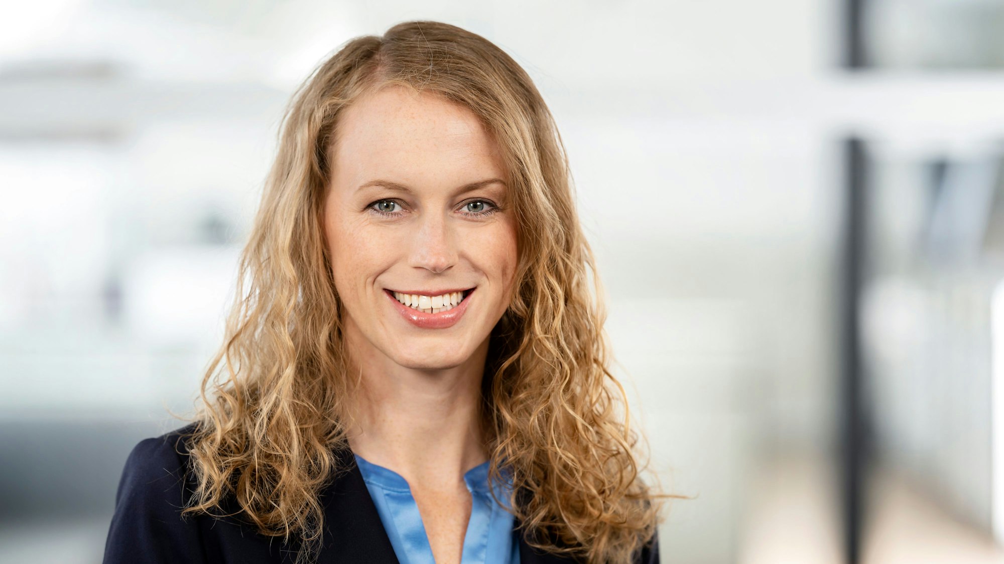 Eine blonde Frau mit Locken lächelt in die Kamera.