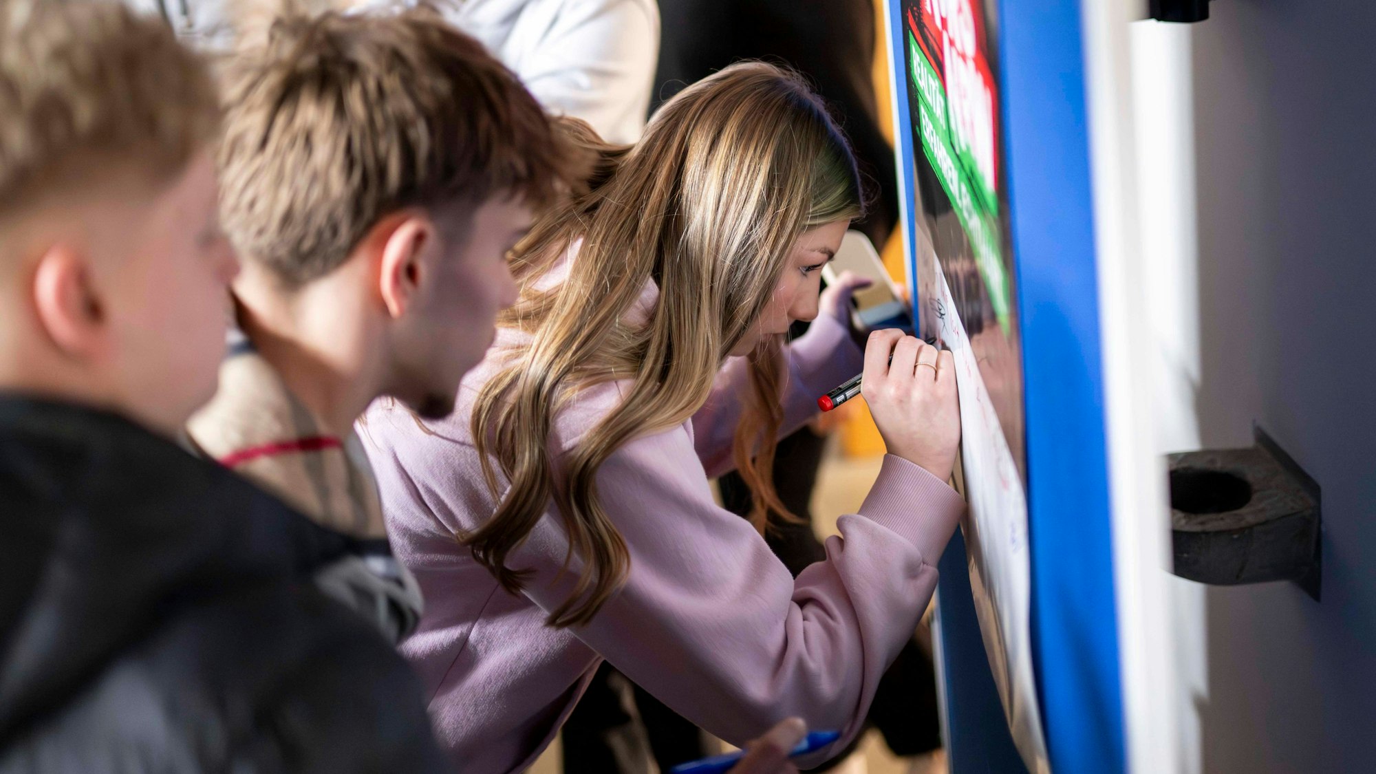Das Bild zeigt eine Schülerin, die auf einem Plakat unterschreibt.