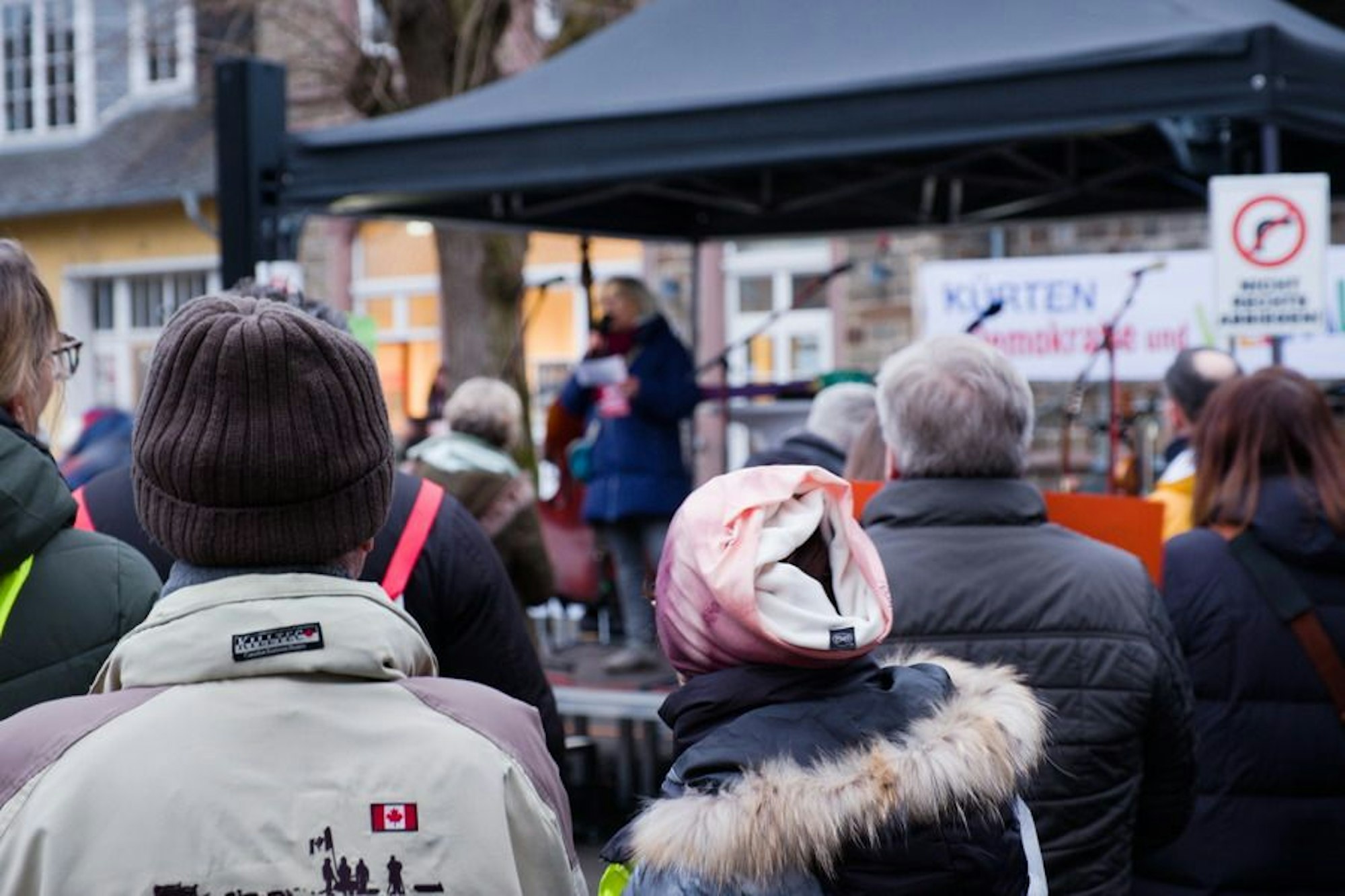 Eine Rednerin steht auf einer Bühne und spricht zu Menschen auf dem Overather Bahnhofplatz.