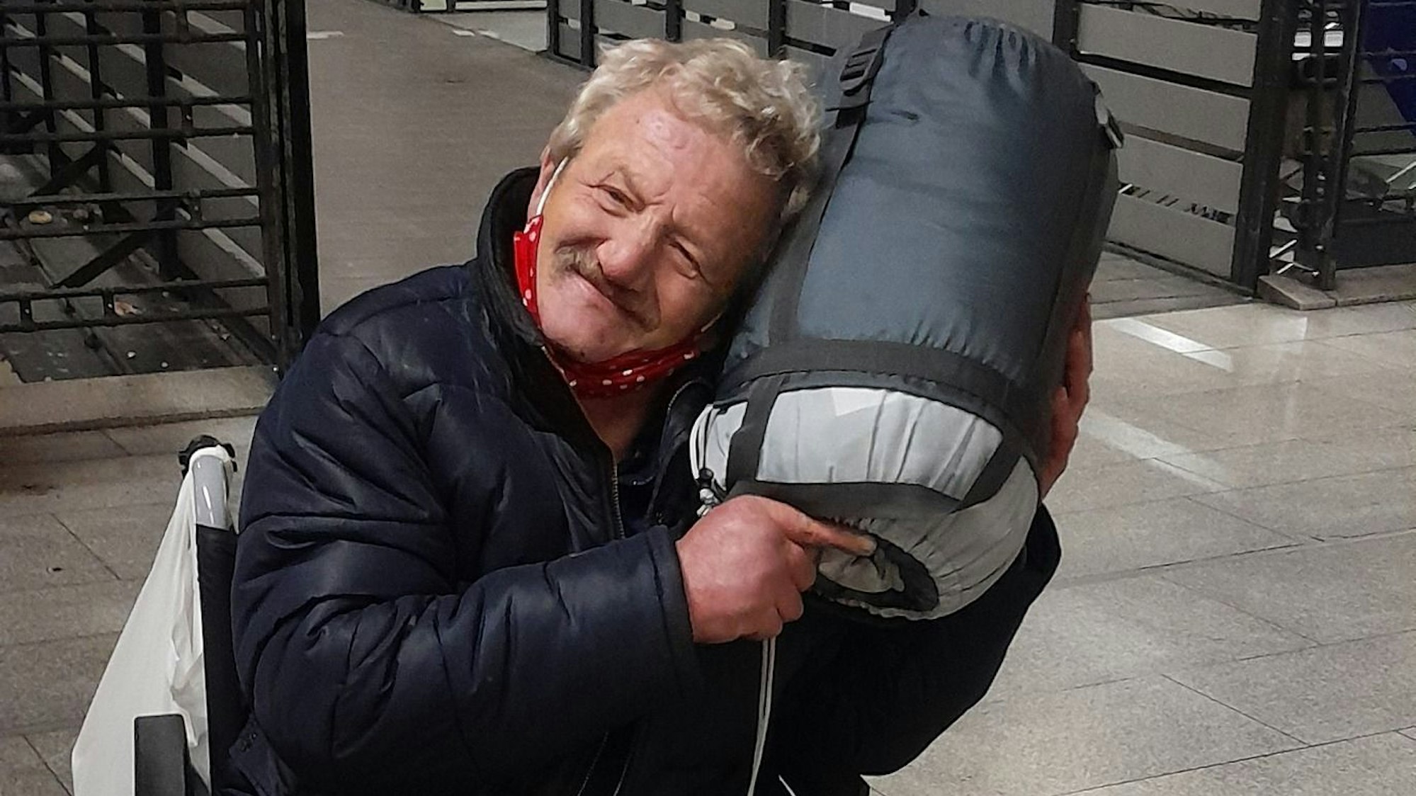 Ein Mann im Rollstuhl kuschelt mit einem aufgerollten Schlafsack.