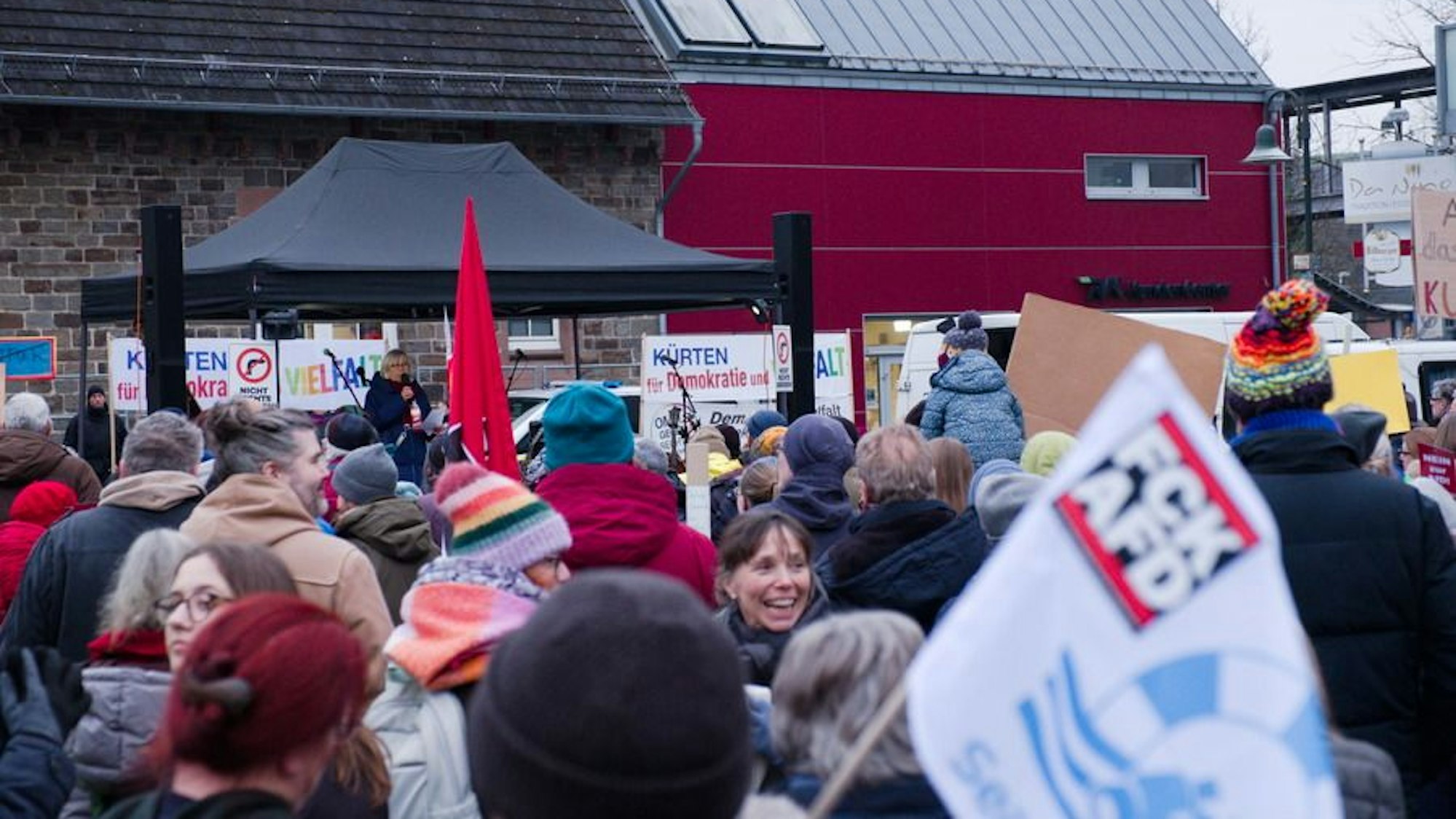 Eine Rednerin steht auf einer Bühne und spricht zu Menschen auf dem Overather Bahnhofplatz.