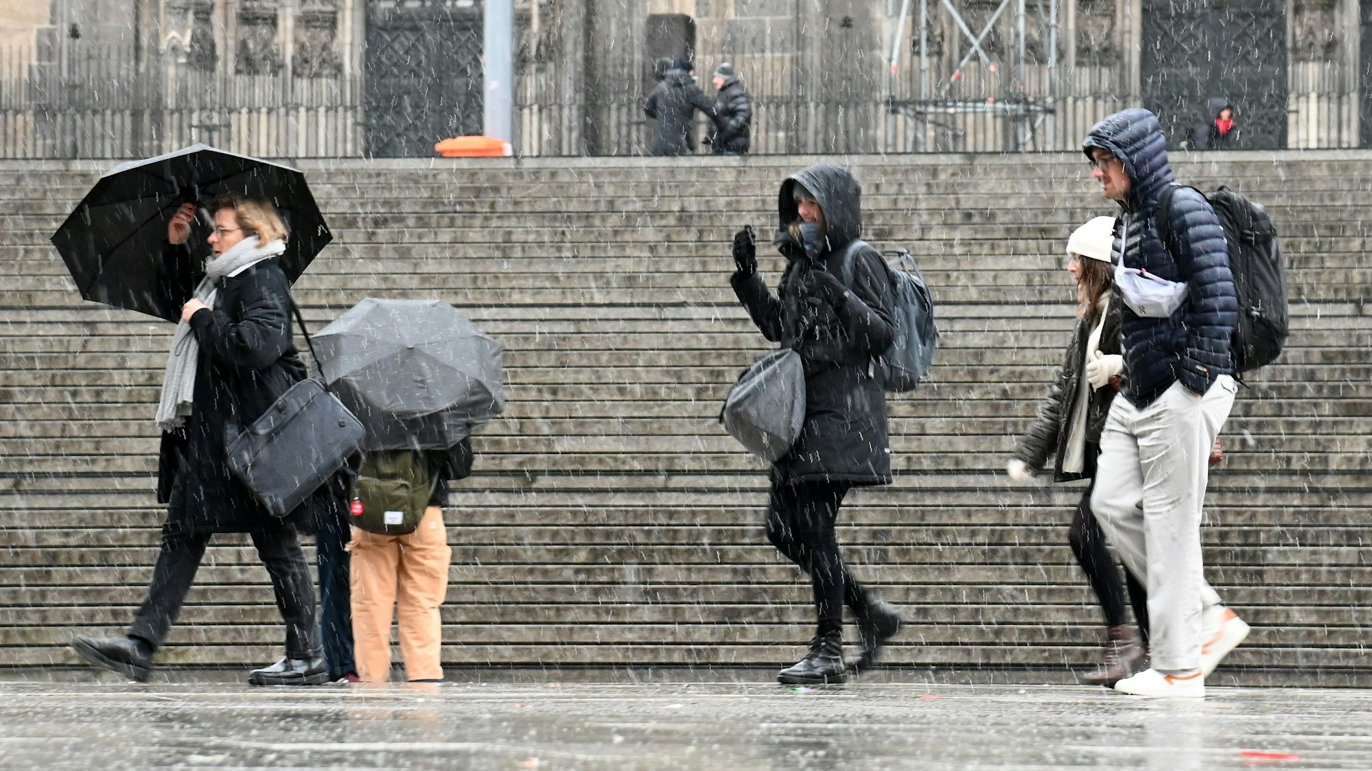Passanten und Passantinnen mit Regenschirmen bei Schneefall vor dem Kölner Dom.
