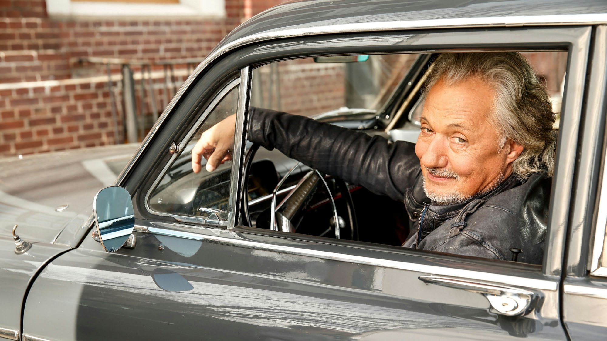 Konrad Beikircher am Steuer eines Autos.