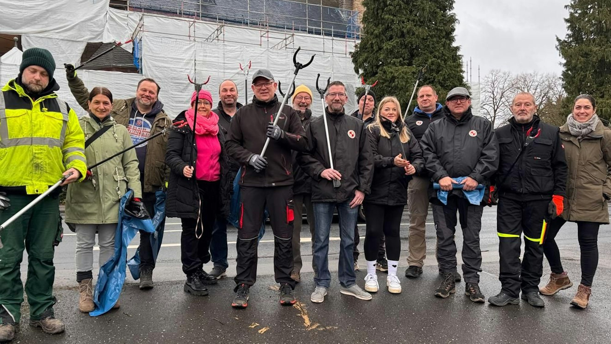 Eine Gruppe Menschen steht, mit Müllsammel-Werkzeug ausgerüstet, an einer Straße