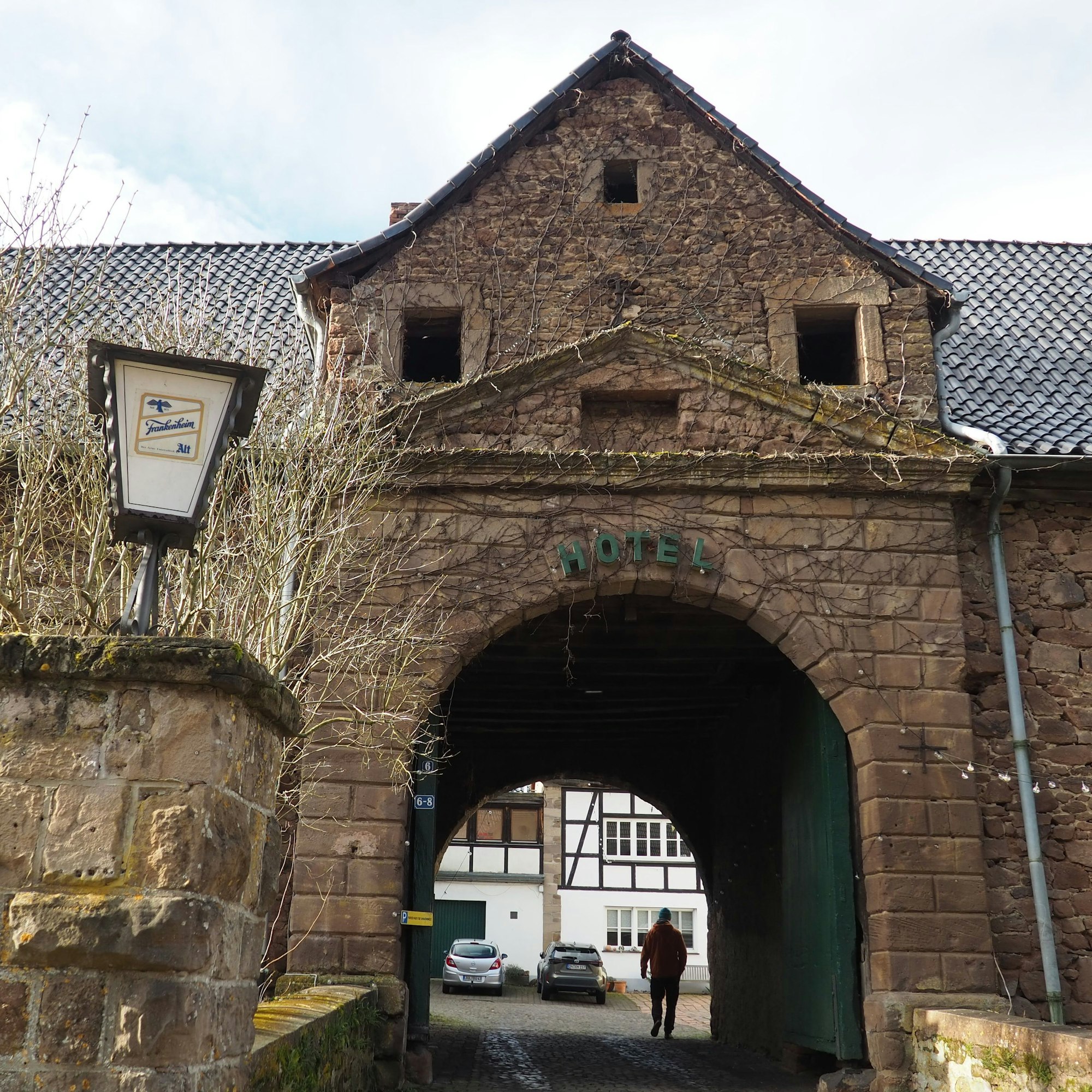 Am historischen Torbogen, durch den ein Mann in den Innenhof geht, prangt ein Schriftzug „Hotel“.