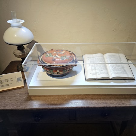 Blick auf eine Vitrine mit einer Wöchnerinnenschüssel und einem aufgeschlagenen Buch.